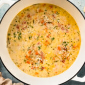 Overhead photo of a large white pot filled with Tuscan White Bean Soup with bacon with a chunk of parmesan and ramekin of salt next to the pot.
