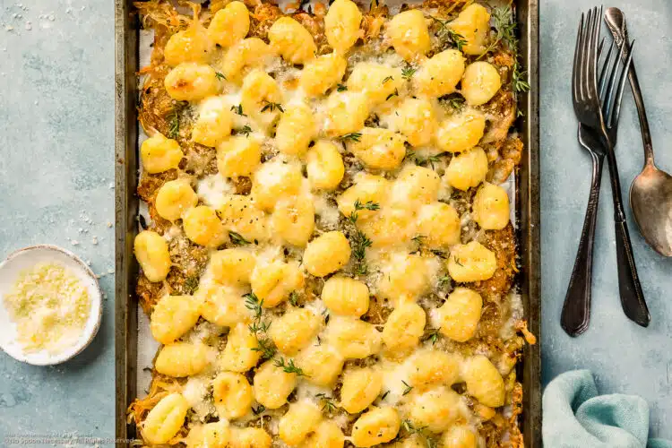 Overhead photo of baked gnocchi with caramelized onions and cheese on a baking sheet.