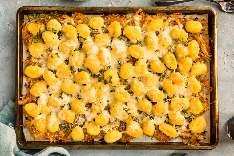Overhead photo of baked gnocchi recipe with caramelized onions, mozzarella cheese, and parmesan cheese on a large sheet pan.