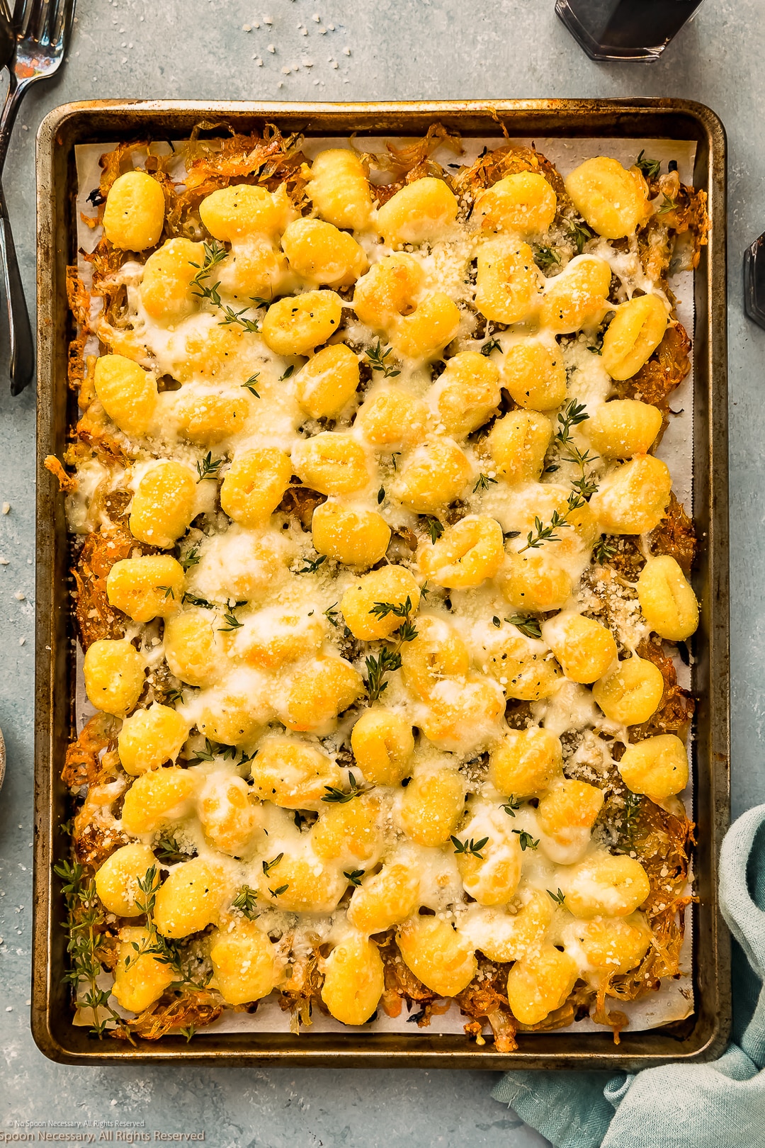 Overhead photo of cheesy gnocchi with french onions, parmesan cheese, and mozzarella cheese on a large baking sheet.