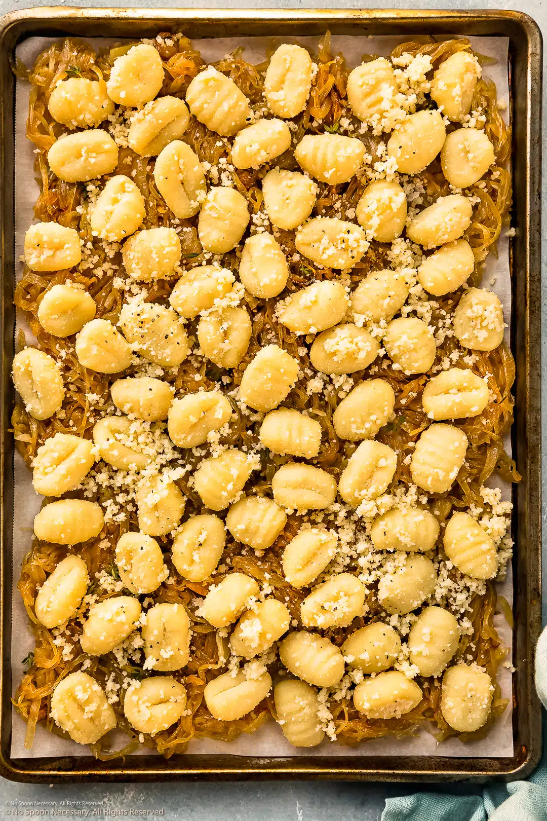 Overhead photo of a sheet pan with caramelized onions topped with potato gnocchi - before baking.
