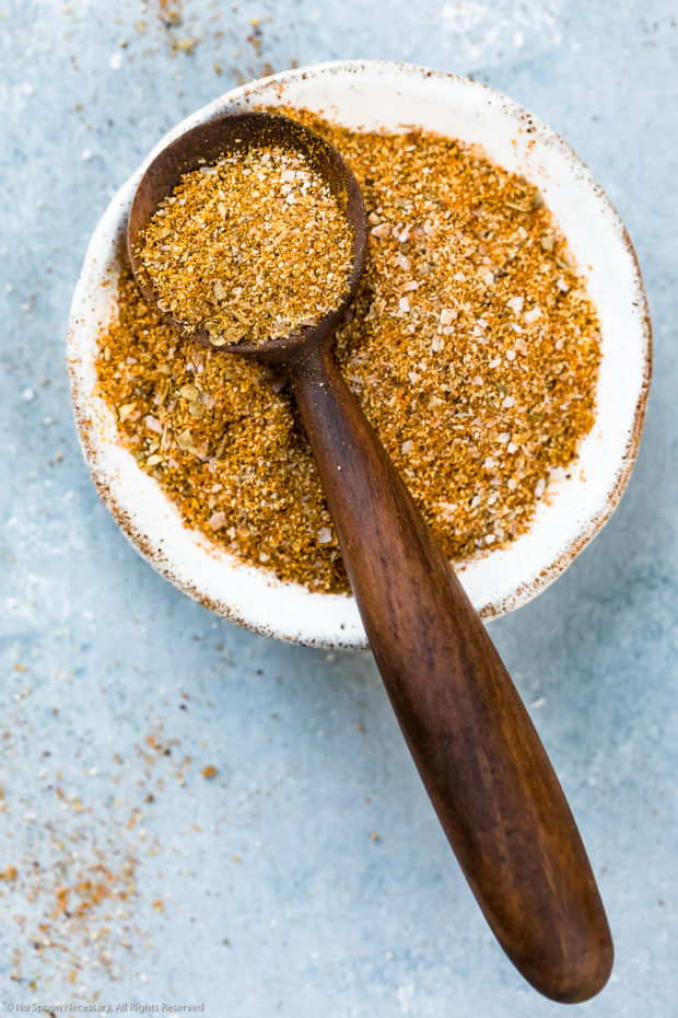 Overhead, vertical photo of Homemade Sazon Seasoning Mix in a ramekin with a small wooden spoon full of seasoning resting on the ramekin.