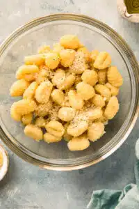 Overhead photo of raw gnocchi with salt and pepper in a large mixing bowl.