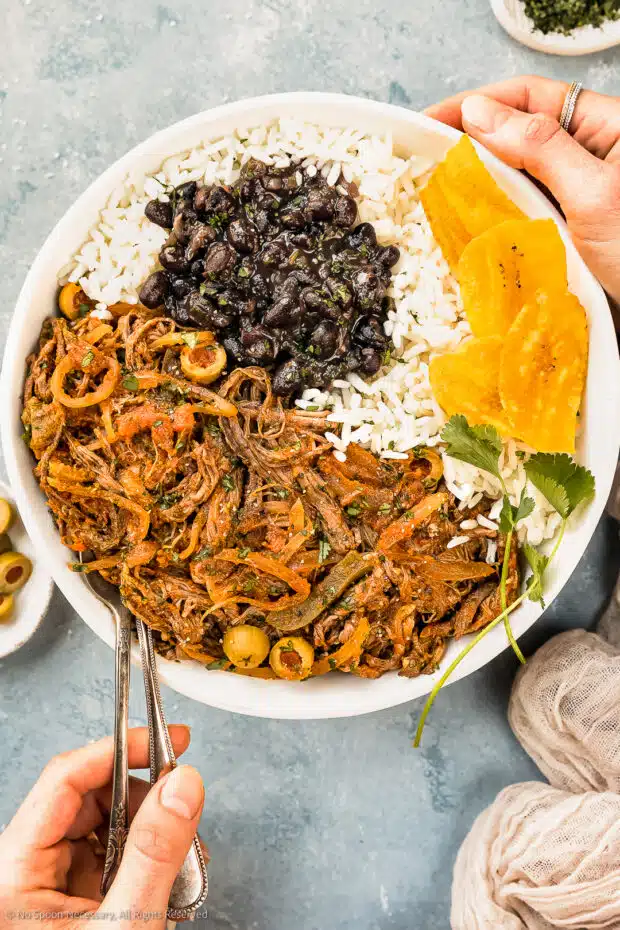 Overhead photo of a bowl of vieja ropa beef with cuban beans, rice and plantains. 