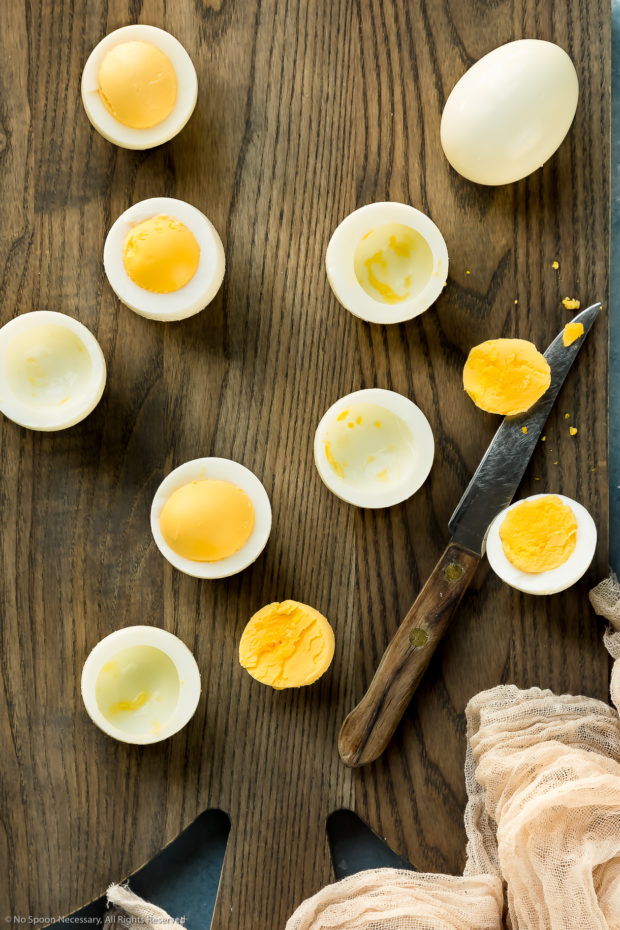 Overhead photo of halved hard boiled eggs on a large wooden cutting board - prep shot of how to make bacon deviled eggs.