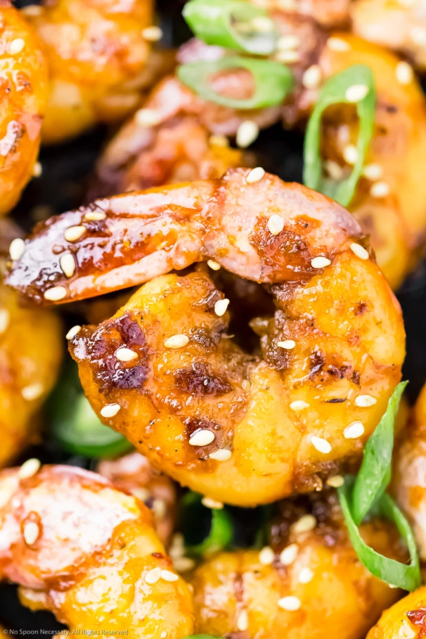 Overhead, extreme close-up photo a honey garlic shrimp garnished with sesame seeds and sliced scallions.