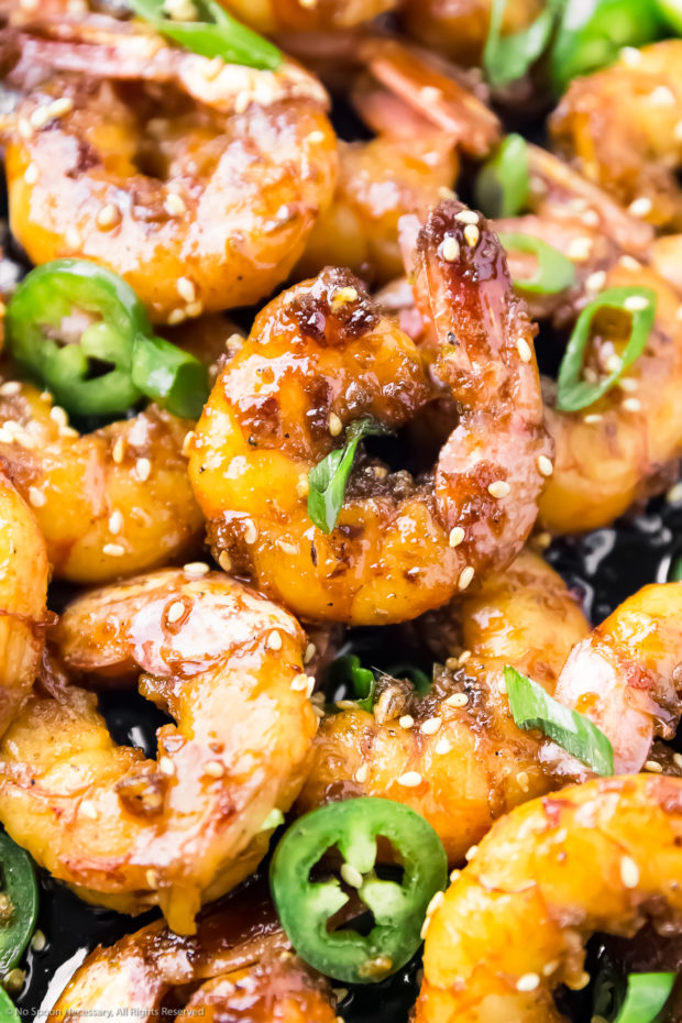Overhead, close- up photo of Shrimp cooked in a honey garlic sauce and garnished with lime wedges, jalapeno slices, and sliced scallions.