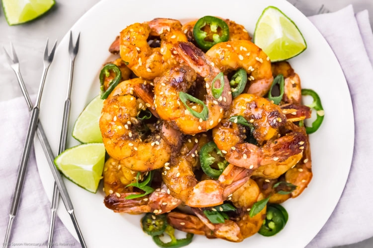 Overhead photo of Honey Garlic Shrimp garnished with scallions and lime wedges on a white plate with more lime wedges next to the plate.