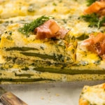 Straight on photo of a slice of eggs and asparagus frittata topped with cheese and herbs.