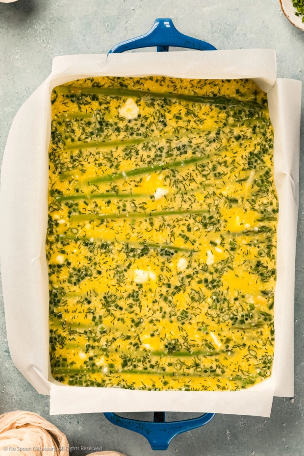 Overhead photo of a parchment paper lined baking dish filled with frittata custard and asparagus (before being baked). 