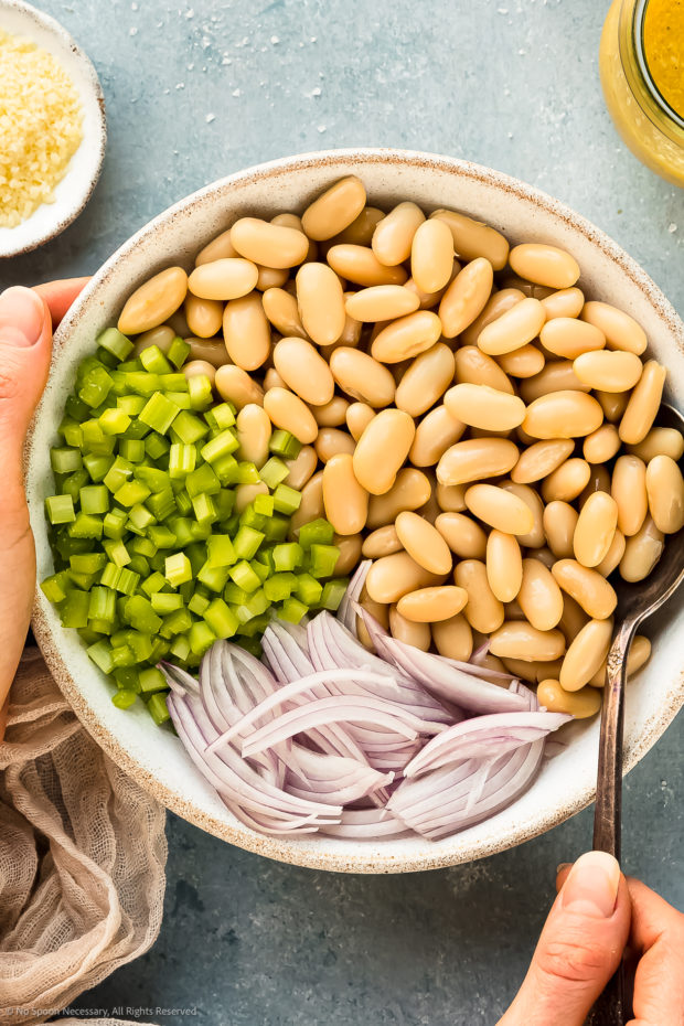 Overhead photo of white kidney beans, chopped celery and sliced scallions in a medium bowl.
