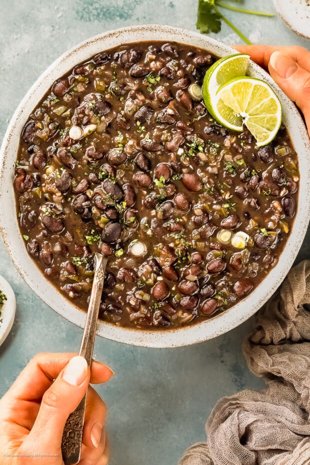 Action photo of a person scooping cuban style black beans from a serving bowl.
