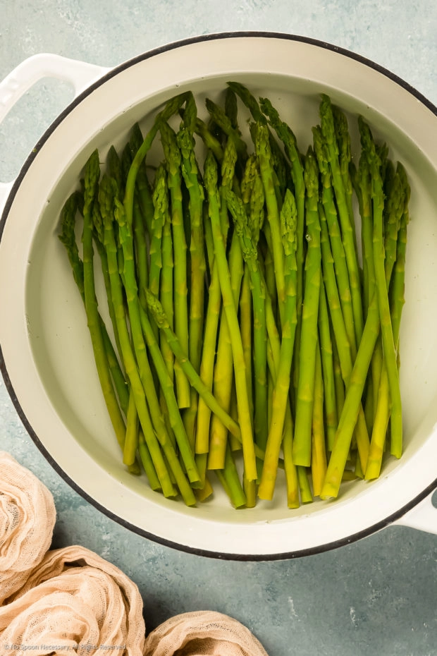 Overhead photo of blanched asparagus in a white pot filled with water.