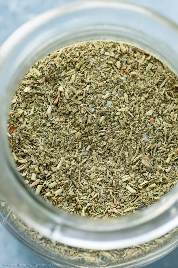 Overhead, up-close photo of Italian spice blend in a small glass jar.