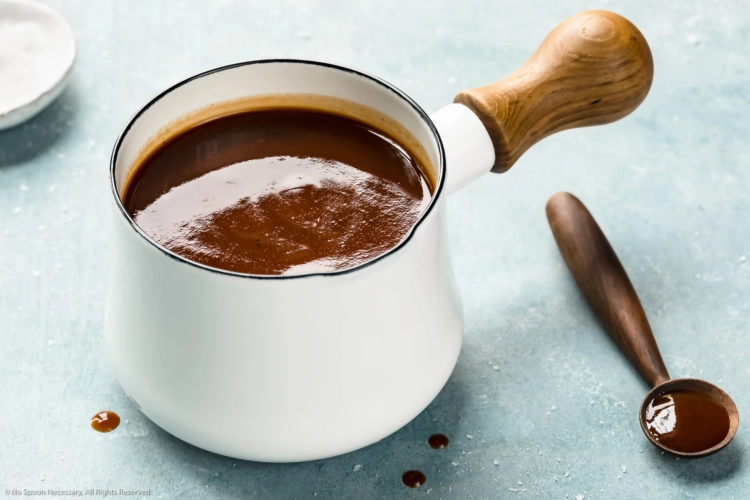 Angled photo of Carolina BBQ sauce in a small white sauce pan with a wooden spoon of sauce off to the side.