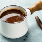Angled photo of Carolina BBQ sauce in a small white sauce pan with a wooden spoon of sauce off to the side.