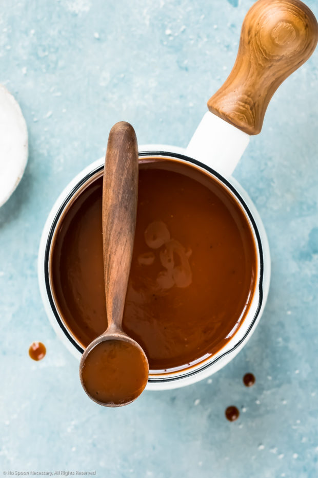 Overhead photo of Carolina BBQ Sauce in a small white sauce pan with a wooden spoon of sauce resting on the top of the pan.