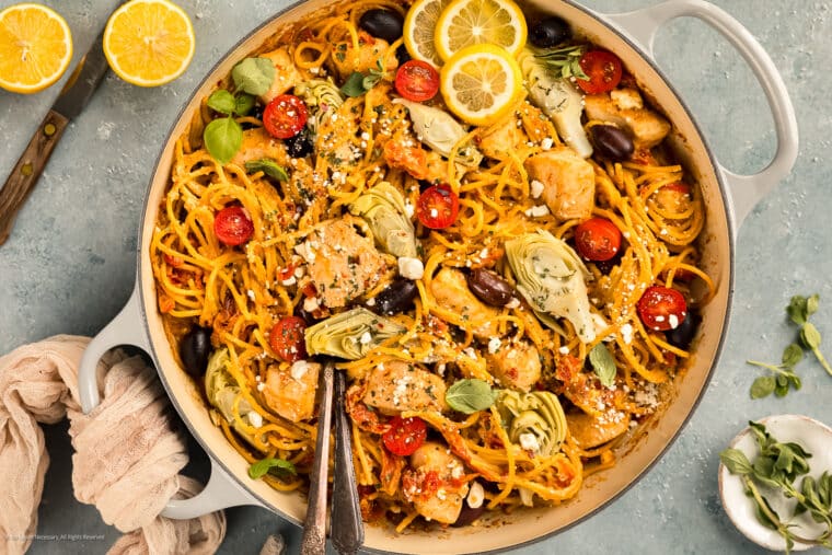 Overhead photo of chicken mediterranean pasta with olives, artichokes, feta, and tomatoes in a large skillet.