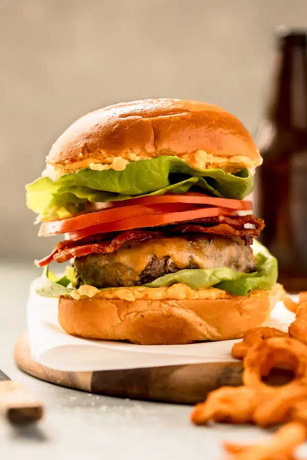 Straight on shot of a cheeseburger made with homemade ground beef and topped with bacon, sliced tomatoes and lettuce.