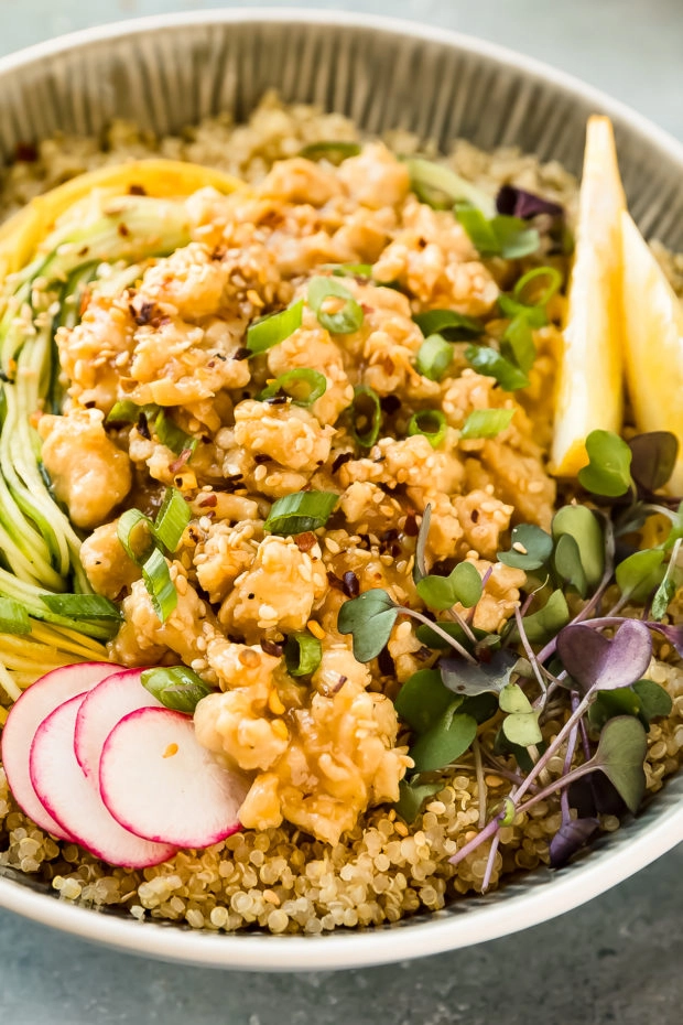 Angled, close-up photo of stir-fried Lemon Chicken served over quinoa and vegetables noodles in a white bowl.