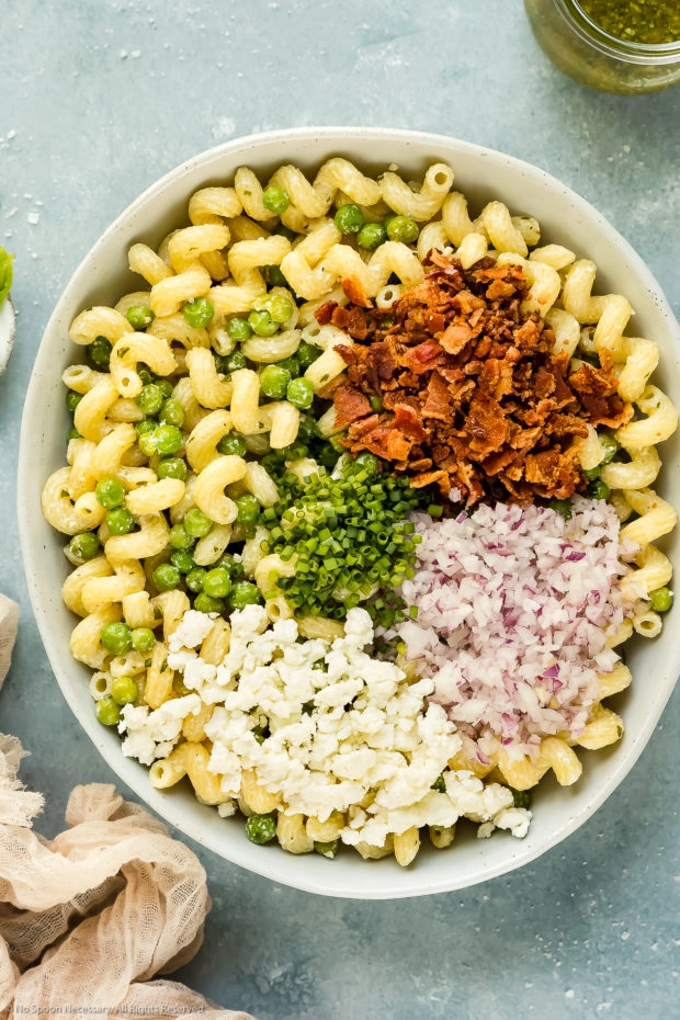 Overhead photo of all the ingredients needed to make bacon pea pasta salad neatly arranged in a large white mixing bowl before being tossed together.