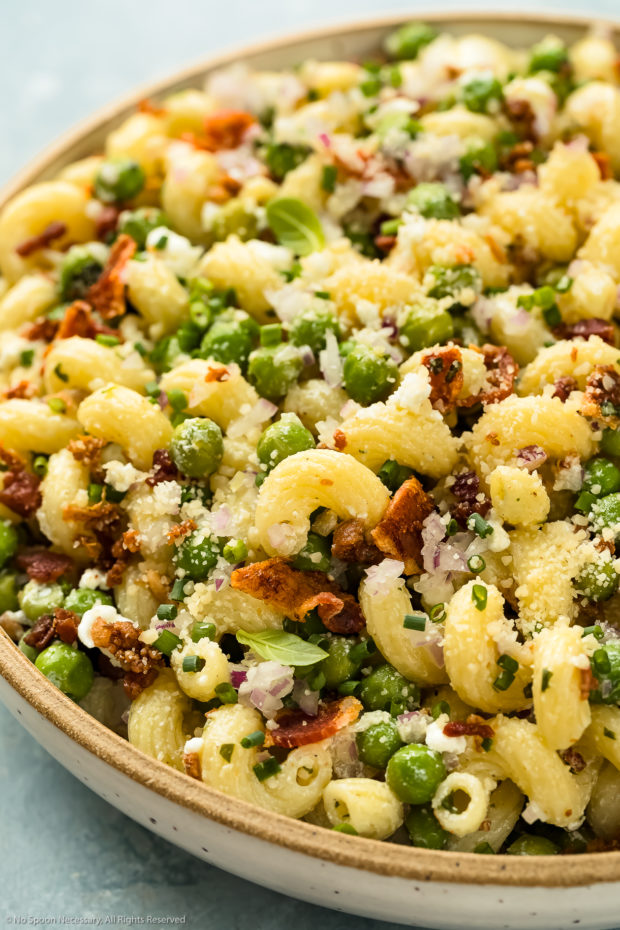 Angled, close-up photo of No Mayo Pasta Salad with peas, bacon and goat cheese in a white serving bowl.