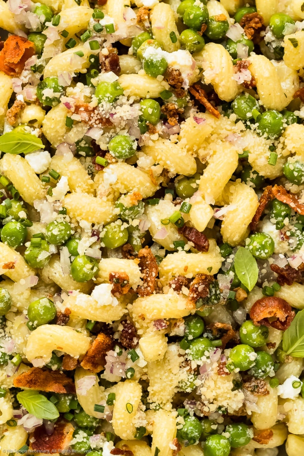 Overhead close-up photo of no-mayo pasta salad with bacon, peas, cheese, red onion and fresh herbs.