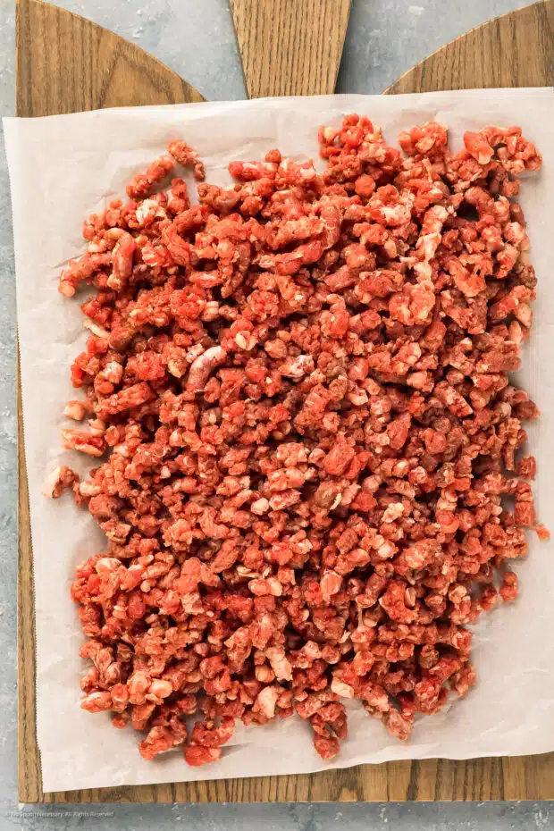 Overhead photo of homemade ground beef on a parchment paper lined wood board.