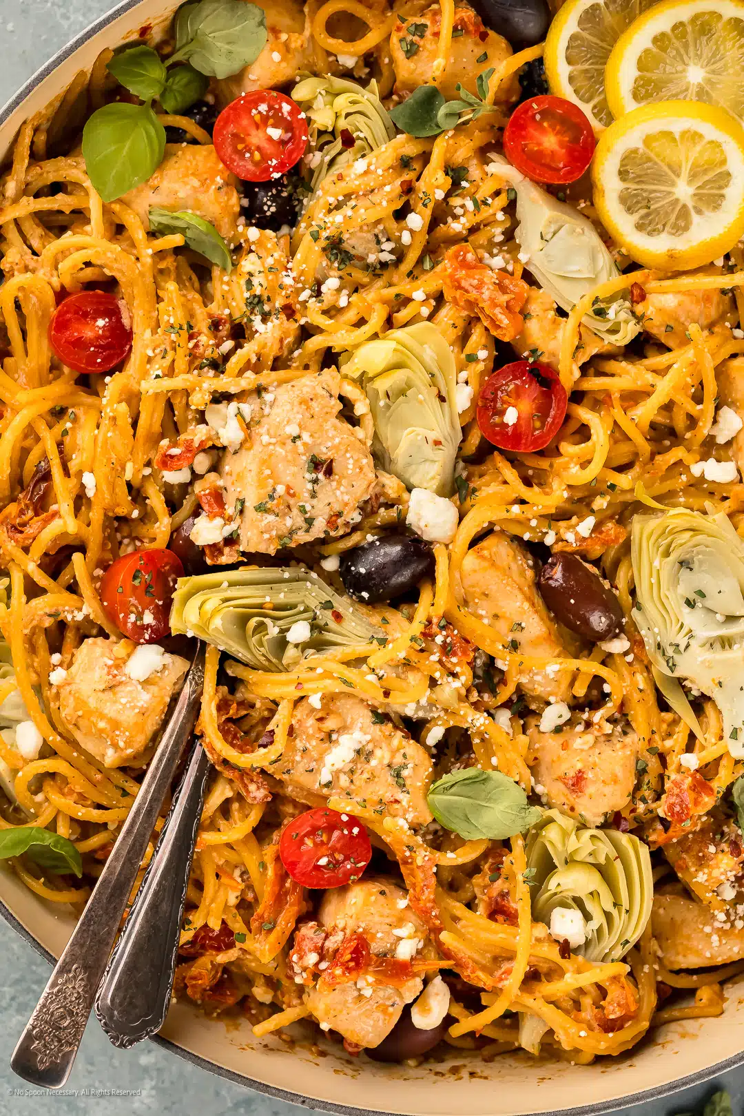 Overhead photo mediterranean chicken pasta with serving spoons inserted into the pasta.