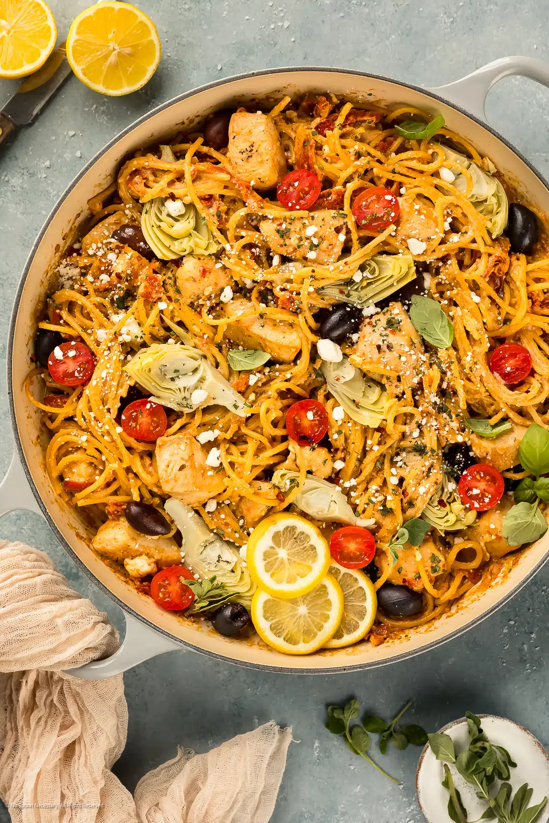 Overhead photo of mediterranean pasta with chicken, sun dried tomatoes, olives, and feta in a large enamel pan.