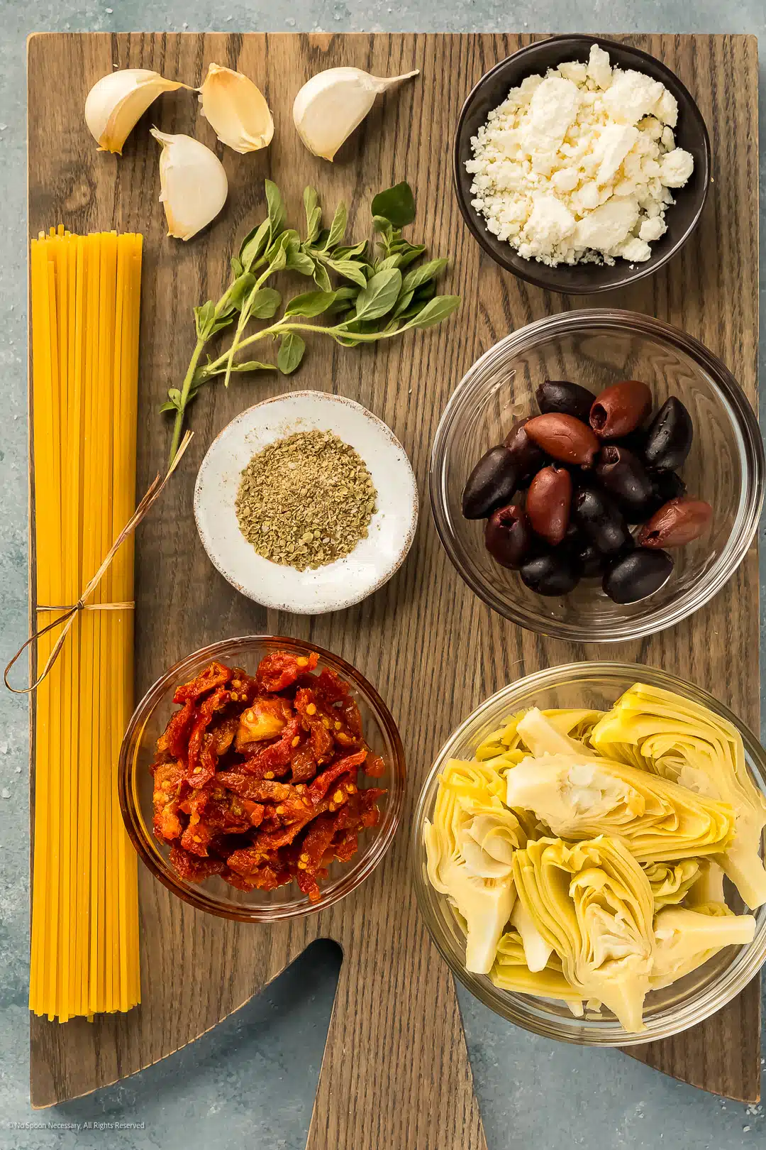 Overhead photo of the eight ingredients in mediterranean pasta recipe neatly arranged on a wood board.