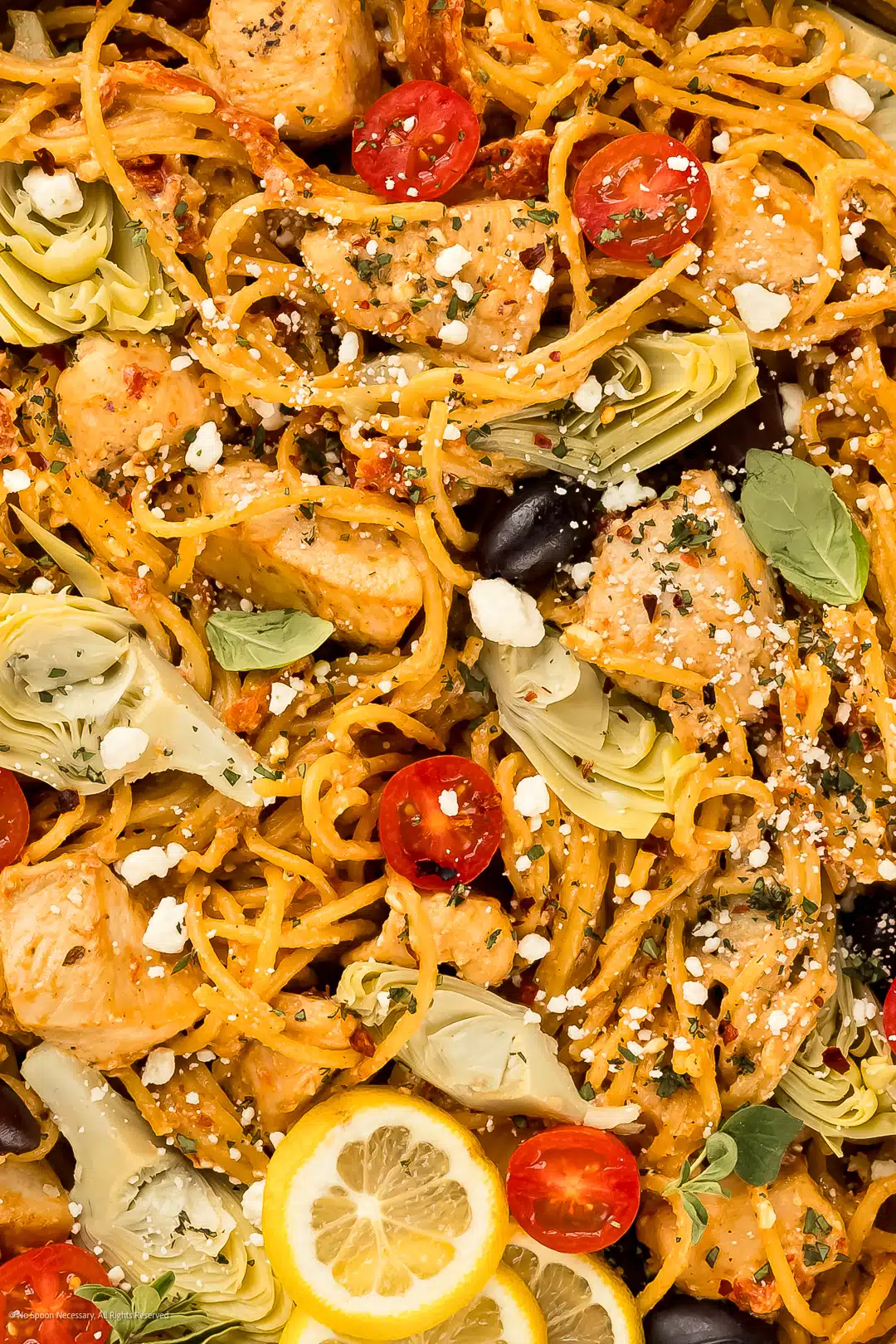 Close-up photo showcasing the texture of mediterranean pasta with chicken breasts, artichoke hearts, olives, and feta.