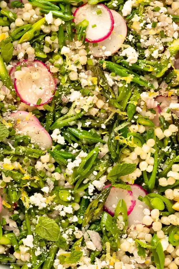 Close-up photo of cooked couscous tossed with a lemon dressing and asparagus.