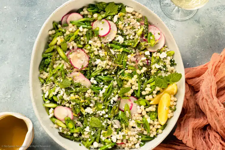 Overhead photo of lemony couscous salad with asparagus in a white serving bowl.