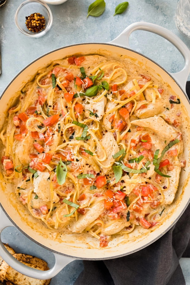 Overhead photo of pasta with chicken, tomatoes and basil in a large gray skillet.