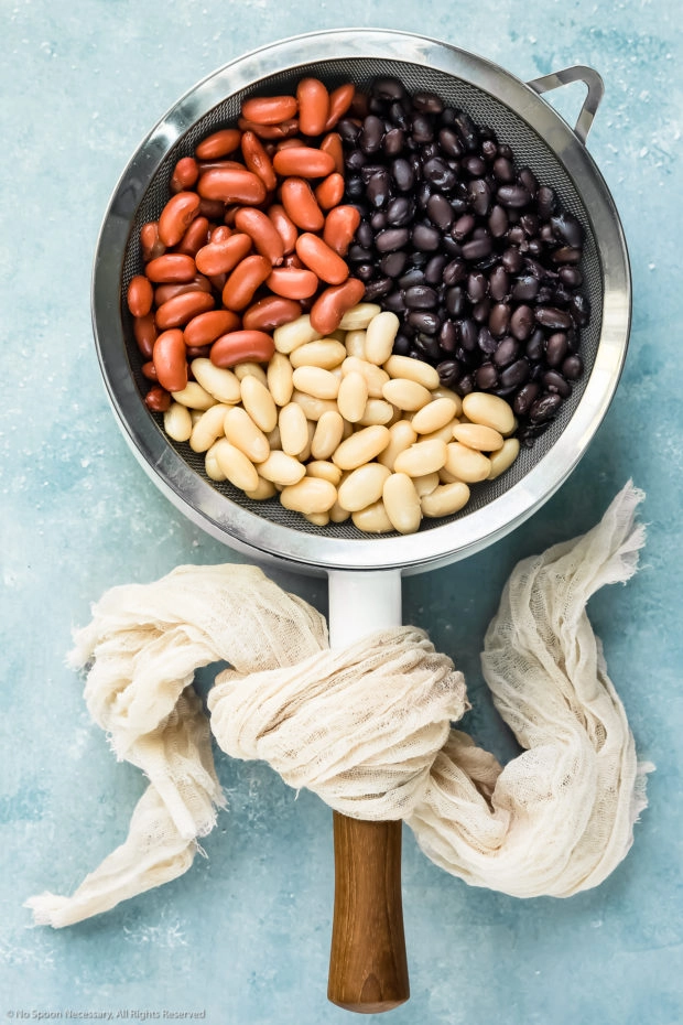 Overhead photo of three types of beans - black beans, white beans and kidney beans - in a strainer inserted over a pot (prep photo for how to make Mexican three bean salad).