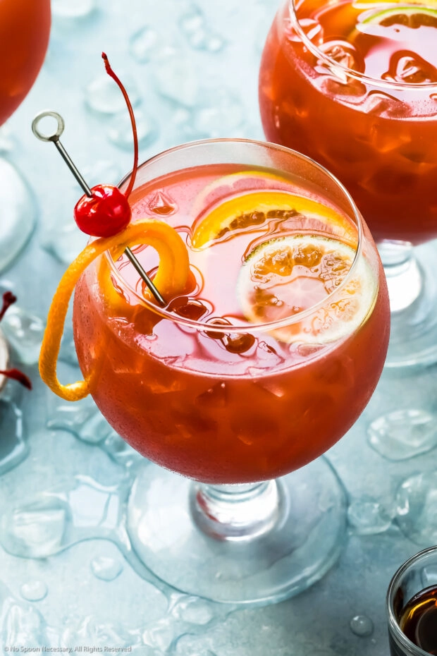Angled photo of a Rum Runner Cocktail garnished with orange and lime slices, and a Maraschino cherry. 
