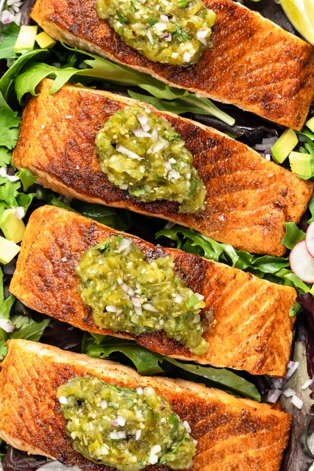 Overhead, up-close photo of pan-seared Salmon garnished with Salsa Verde on a bed of greens. (Photo of how to serve salmon with salsa)