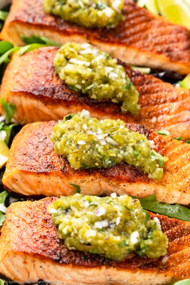 Angled photo of pan-seared Salmon garnished with Salsa Verde on a bed of greens. 