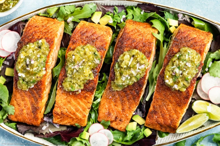 Overhead photo of a white platter topped with pan-seared Salmon garnished with Salsa Verde on a bed of greens.