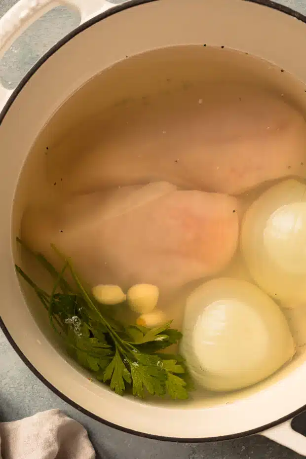 Overhead photo of two raw chicken breasts poaching in a large pot of water.