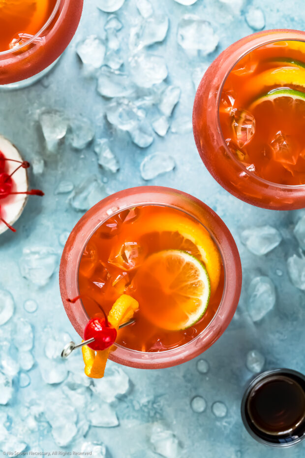 Overhead photo of two Rum Runner drinks garnished with lime, orange and maraschino cherries.