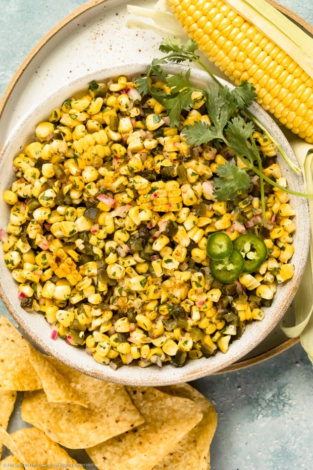 Overhead photo of Sweet Corn Salsa with peppers, onions and cilantro in a large white bowl with an ear of corn and tortilla chips next to the bowl.