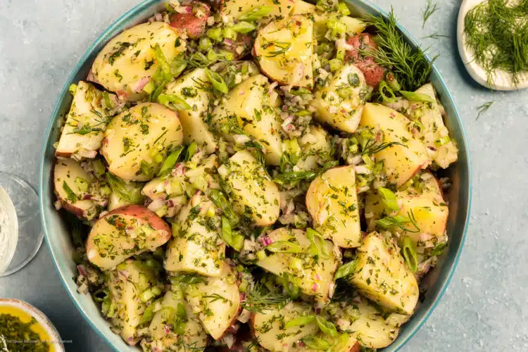 Overhead photo of a no mayo potato salad with fresh herbs and olive oil dressing in a large serving bowl.