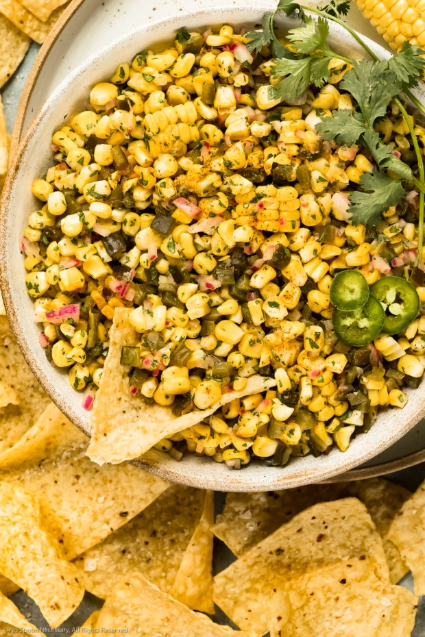 Overhead photo of Sweet and Spicy Corn Salsa a large white bowl with a tortilla chip inserted into the salsa.