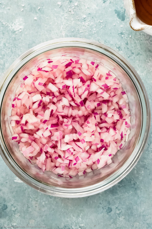 Overhead photo of finely diced red onions tossed with vinegar in a small glass bowl - photo of step 1 of recipe.