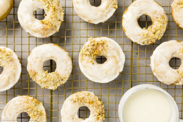 Overhead photo of Baked Apple Cider Donuts on a a gold wire rack with a ramekin of glaze tucked into the corner of the shot.