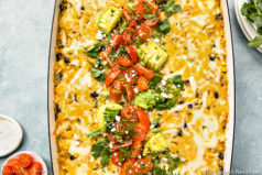 Overhead, landscape photo of a Chicken Mexican Casserole topped with melty cheese, sliced avocados and diced tomatoes.
