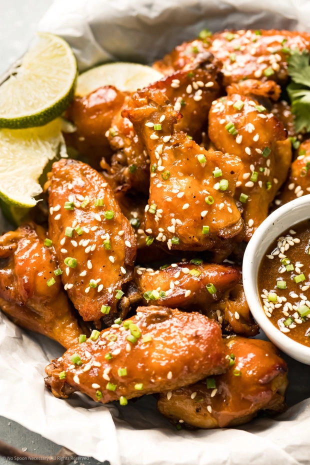 Angled photo of baked chicken wings coated in a sticky Chinese sauce with sesame seeds and chives. 
