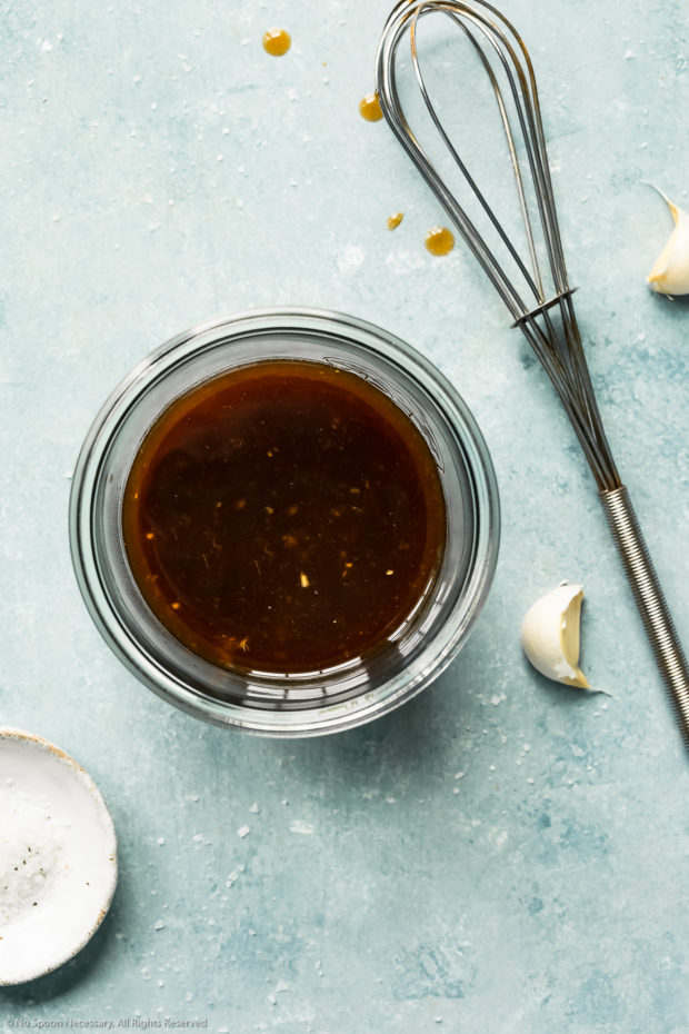 Overhead photo of Chinese chicken wing marinade and sauce in a glass bowl with a wire whisk and cloves of garlic next to the bowl.